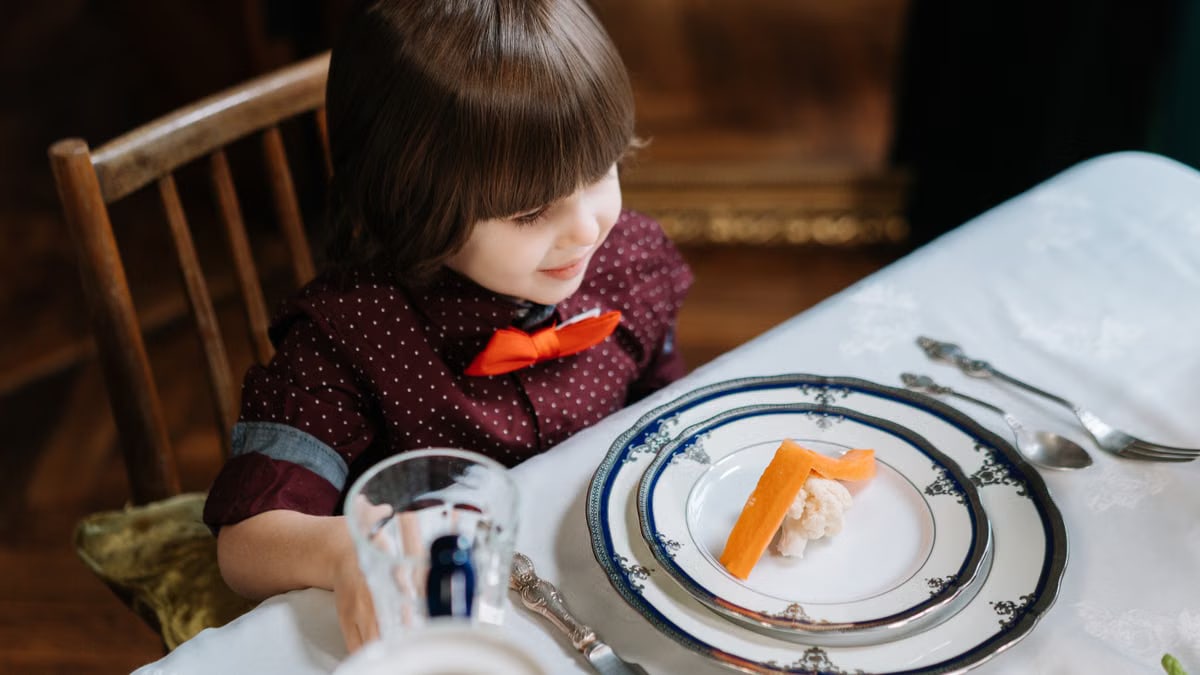 A young child wearing a bow tie seated at a beautifully set dining table.